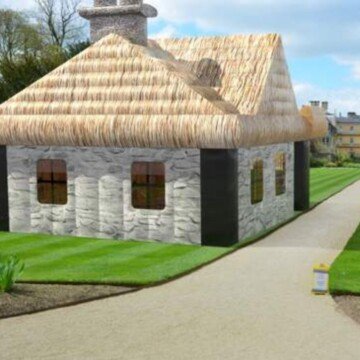 A thatched cottage blow up tent in field beside a paved path
