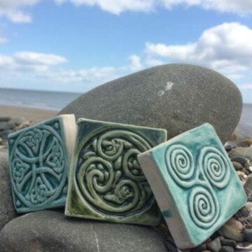 Three Celtic design tiles sitting on a rock by the ocean