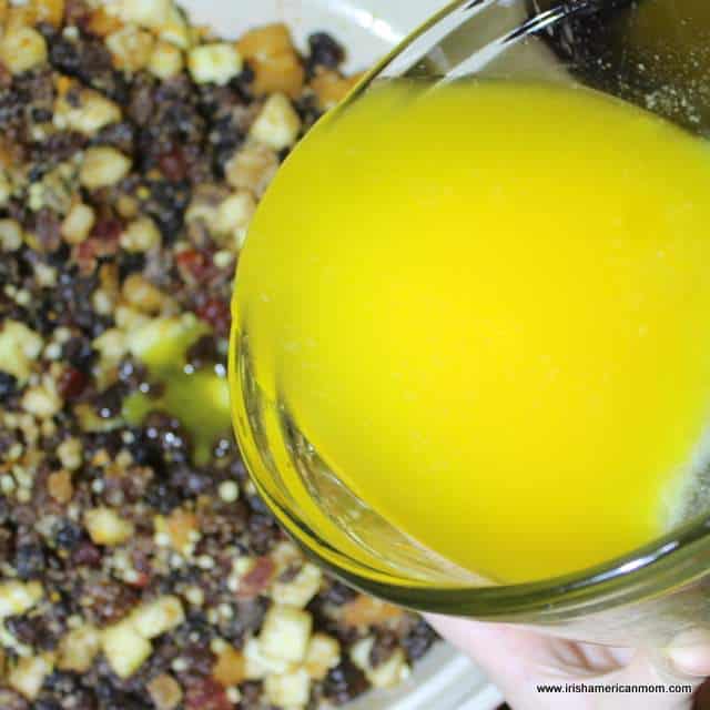 Adding butter rather than suet to mincemeat pie filling | Irish American Mom Adding melted butter to dried fruit in a bowl for festive mince pie filling.