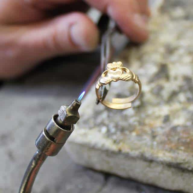 A skilled jeweler using a hot torch to shape and form a Claddagh ring