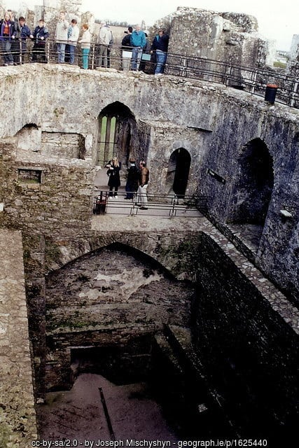 Interior of Blarney Castle with tourists in line to kiss the Blarney Stone | Irish American Mom Interior view of a stone castle with people on a ledge