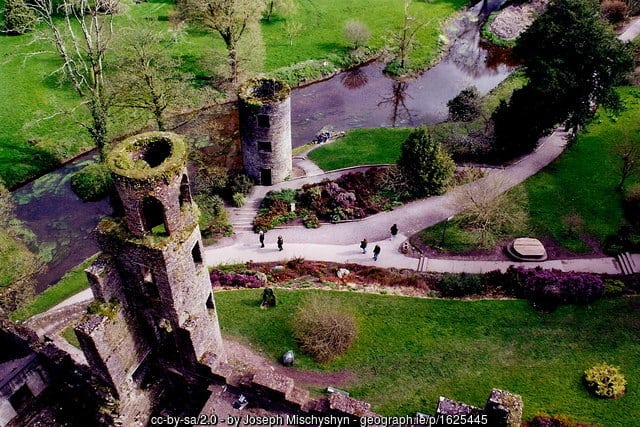 The view from on top of Blarney Castle | Irish American Mom Aerial view of stone towers and people on a path by a river and green fields