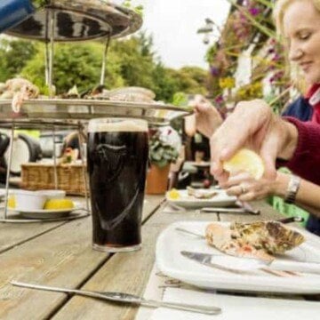 A pint of stout on a wooden table as a lady squeezes a lemon over salmon