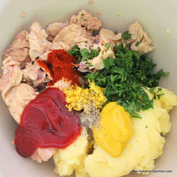 Easy and budget friendly salmon fish cake ingredients ready for mixing in a bowl | Irish American Mom Salmon, ketchup, mustard, mashed potatoes and parsley in a bowl