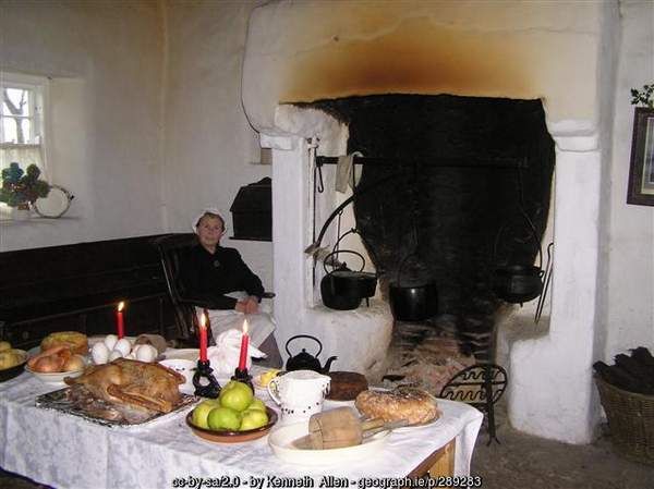 Open Hearth in an old Irish homestead | Irish American Mom A woman beside a fire and a table laid with food