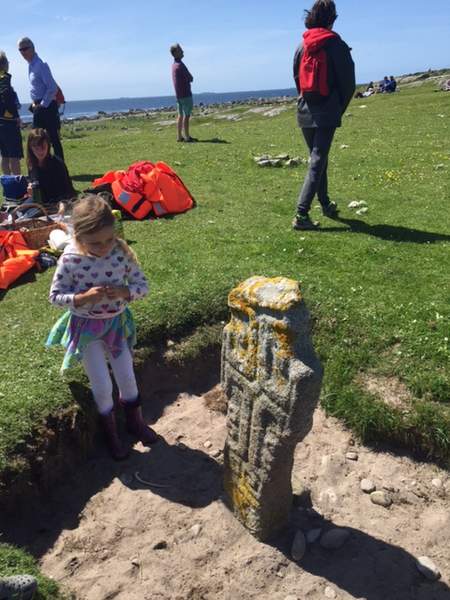 St Macdara stone | Irish American Mom A group of people walking in a field with a child kneeling beside a stone cross