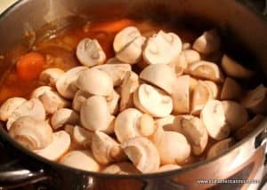 Halved mushrooms being added to a pot of stew