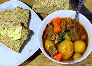 A bowl of stew with a spoon beside a plate of buttered soda bread