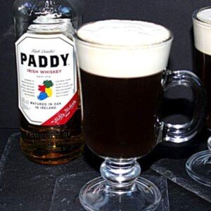 Glass of Irish coffee with a top layer of cream beside a bottle of whiskey