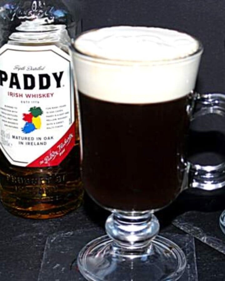 Glass of Irish coffee with a top layer of cream beside a bottle of whiskey