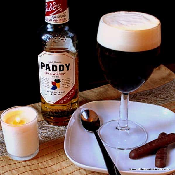 Irish coffee made with Irish whiskey | Irish American Mom A close up of a bottle of whiskey and a glass of Irish coffee with a candle