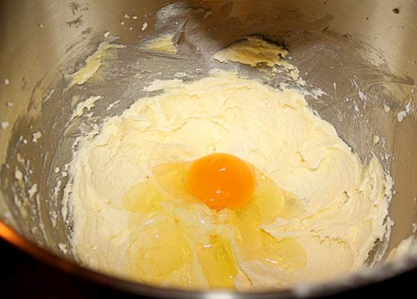 Adding egg to butter and sugar for Eve's Pudding | Irish American Mom An egg being added to creamed butter and sugar in a mixing bowl.