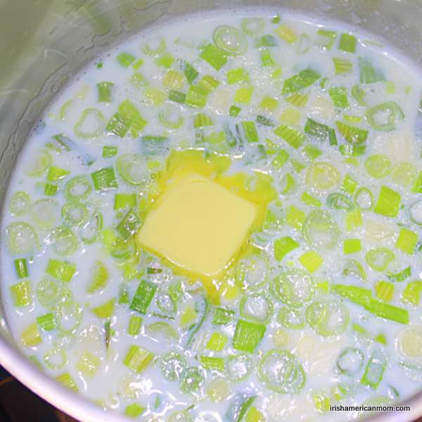Adding butter to milk and scallions for Irish champ | Irish American Mom Butter melting in milk with chopped green onions in a pot