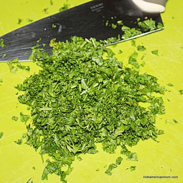 Chopped fresh parsley for parsley sauce | Irish American Mom Fresh parsley chopped beside a knife on a chopping board.