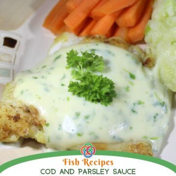 Flaky cod fillet topped with creamy parsley sauce and garnished with fresh parsley, served with carrots and vegetables on a plate.