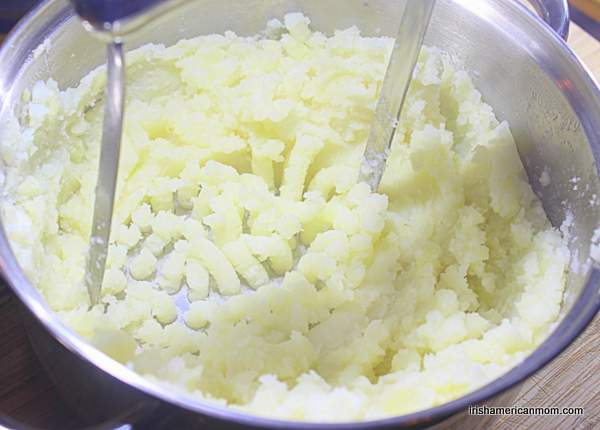 Mashing peeled boiled potatoes for Irish champ | Irish American Mom Using a potato masher to smush potatoes in a pot