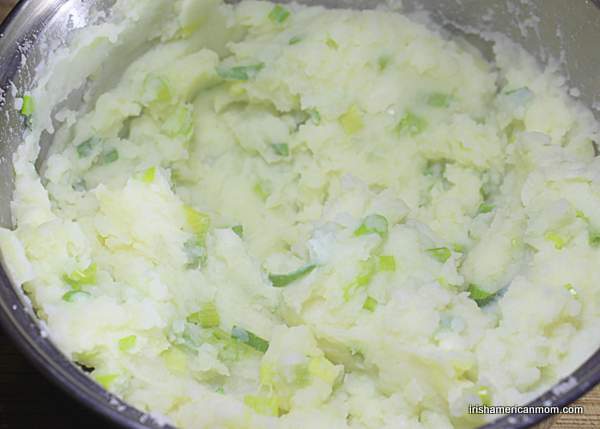 Mixing scallions or green onions, milk, potatoes and butter for Irish champ | Irish American Mom A pot of mashed potatoes with green onions speckled through them