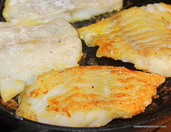 Turning cod fillets in a frying pan | Irish American Mom Golden fried cod fillets being turned for cooking in skillet.