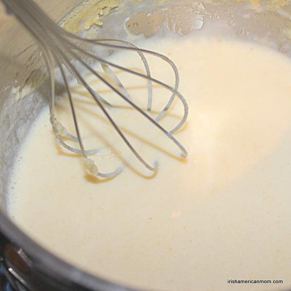 Whisking parsley sauce as it thickens | Irish American Mom Whisking a white sauce with a balloon whisk as it thickens in a saucepan.