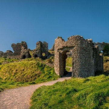 A stone arched entry way on a hill leading to a ruined stone structure
