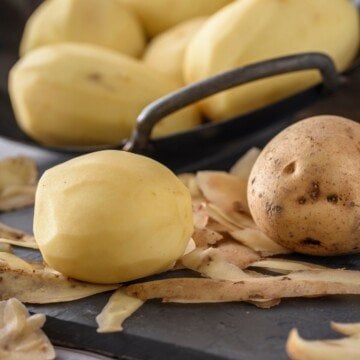 Peeled potatoes in a dish beside potato peels