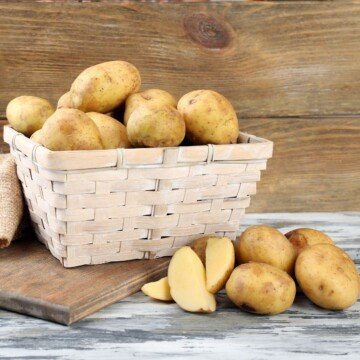 Potatoes beside a cutting board with a basket of potatos