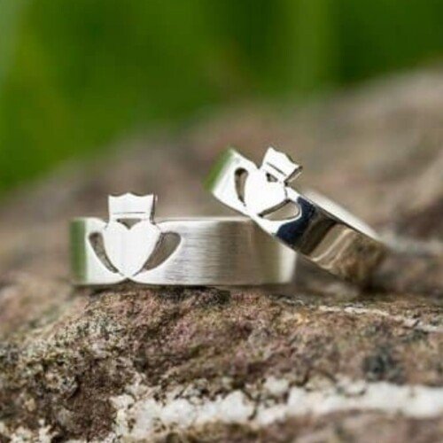 Two wedding bands featuring hearts with crowns displayed on a rock