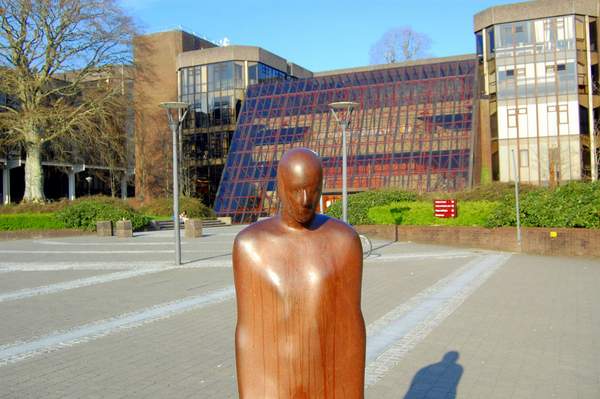 a sculpture of a person in front of a glass university building