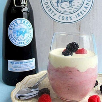 Pink mousse with cream and berries in a glass beside a bottle of Irish cream liqueur