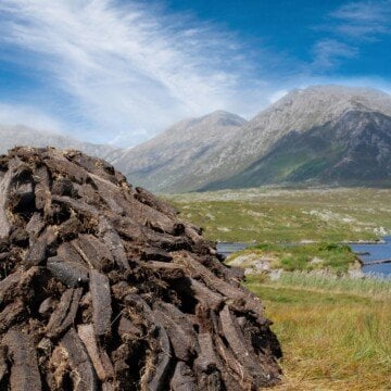 Stack of peat turf in a field beside mountains