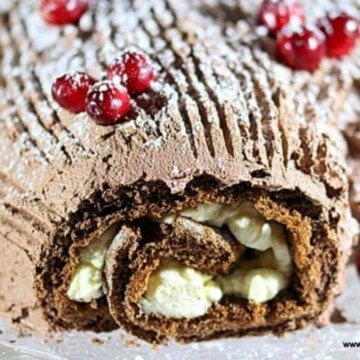 A chocolate roll up cake with whipped cream and chocolate frosting and cranberry decoarations