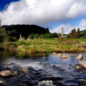 A river by a field with a stone tower and a mountain