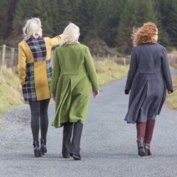 Three women wearing tweed coats walking down a road