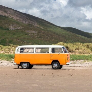 Orange and white vintage minivan beside a mountain slope
