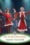 Two performers in red Santa outfits on stage, smiling and waving, with a gift box between them; festive pantomime scene.