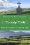 Stone Celtic cross overlooking green fields with sheep and a coastal ocean view on the Beara Peninsula in County Cork, Ireland.