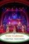 Colorful theatre stage scene with a large cast in festive costumes, Christmas trees, and bright lighting and poster reads 'Irish Traditions Christmas Pantomimes'