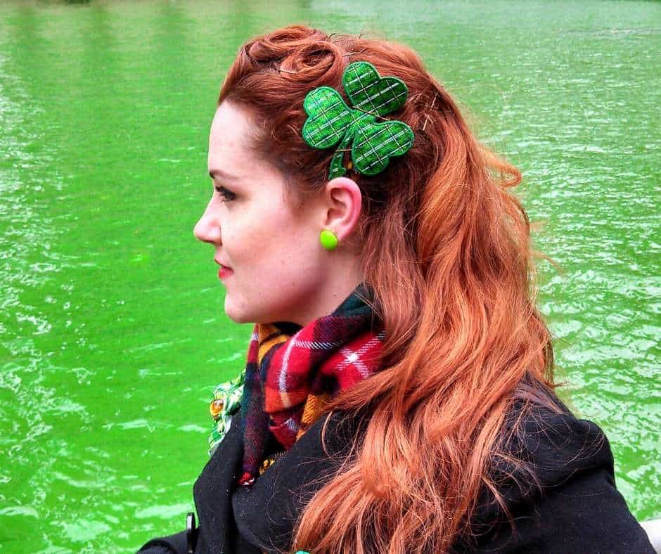 Dying the river green in Chicago | Irish American Mom A red haired Irish lady wears a green shamrock hair accessory by a river dyed green