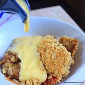 A blue pitcher pouring yellow custard over a serving of rhubarb crumble in a white bowl