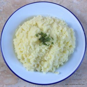 A blue rimmed enamelware bowl of mashed potatoes with green garnish