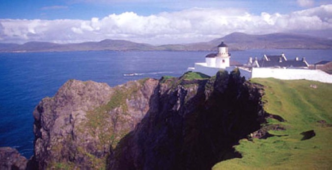 A white lighthouse on top of craggy cliffs by the ocean