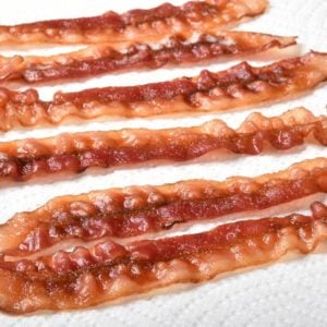 A row of cooked crispy bacon draining on white paper towels