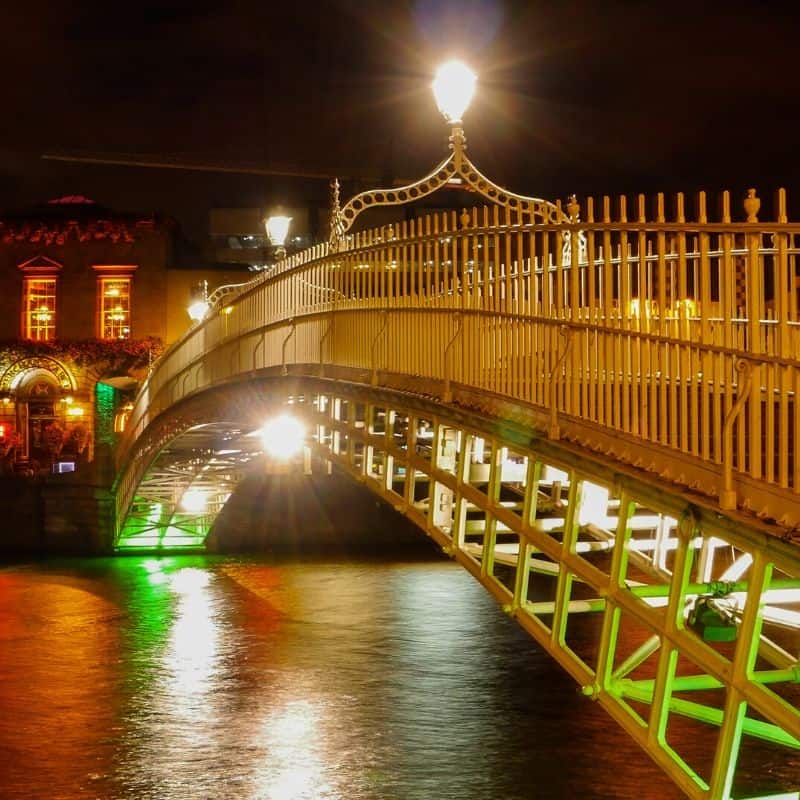 Green lights shining on an arched metal bridge over a river at night