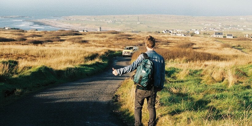 Hitching-feature-backcover-panorama | Irish American Mom A man on the grassy verge of a road thumbing a lift from an approaching van