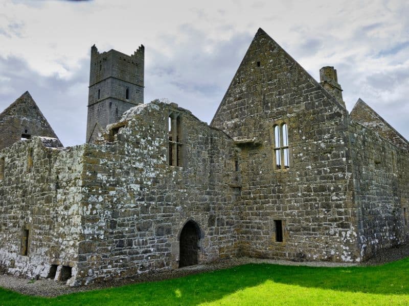 Roofless ruin of a gray stone church with arched doors and green grass