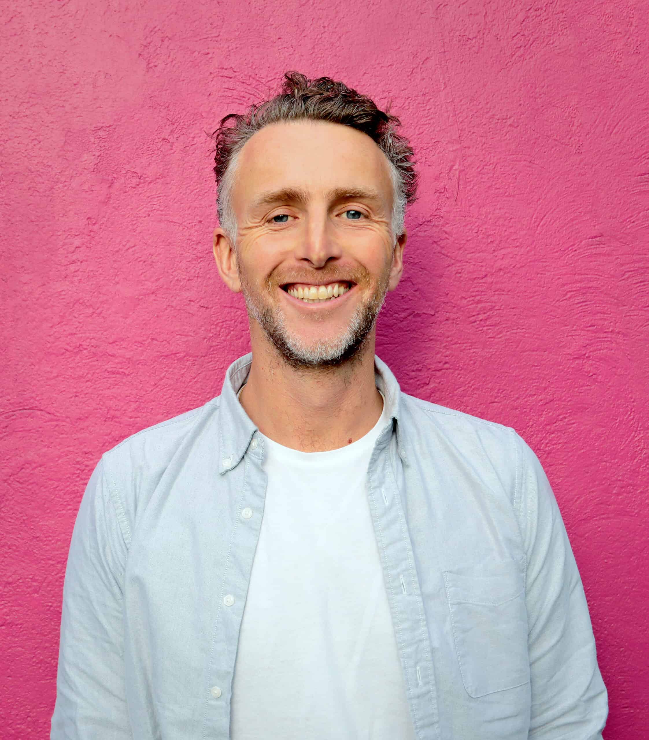 Photo portrait of Ruairi McKiernan with a beard and wearing a white t-shirt and denim shirt