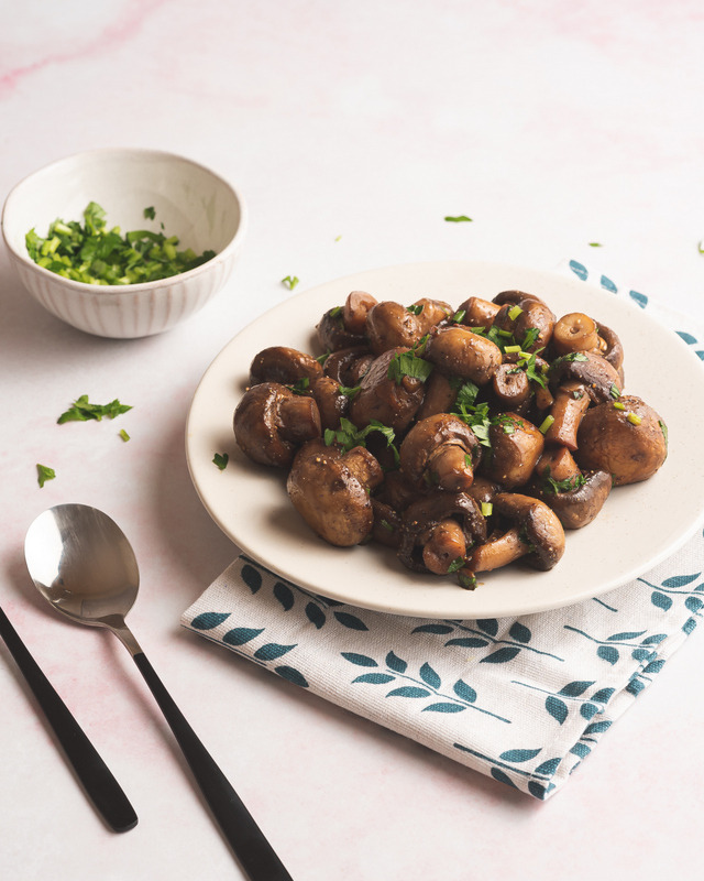 Garlic sauteed mushrooms in a white bowl | Irish American Mom Fried mushrooms on a white dish with a bowls of parsley an a spoon