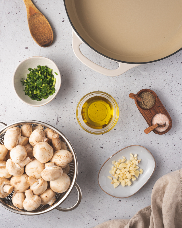 Ingredients for making sauteed garlic mushrooms | Irish American Mom Mushrooms, oil, salt, pepper, minced garlic and parsley beside a skillet for making sautéed garlic mushrooms
