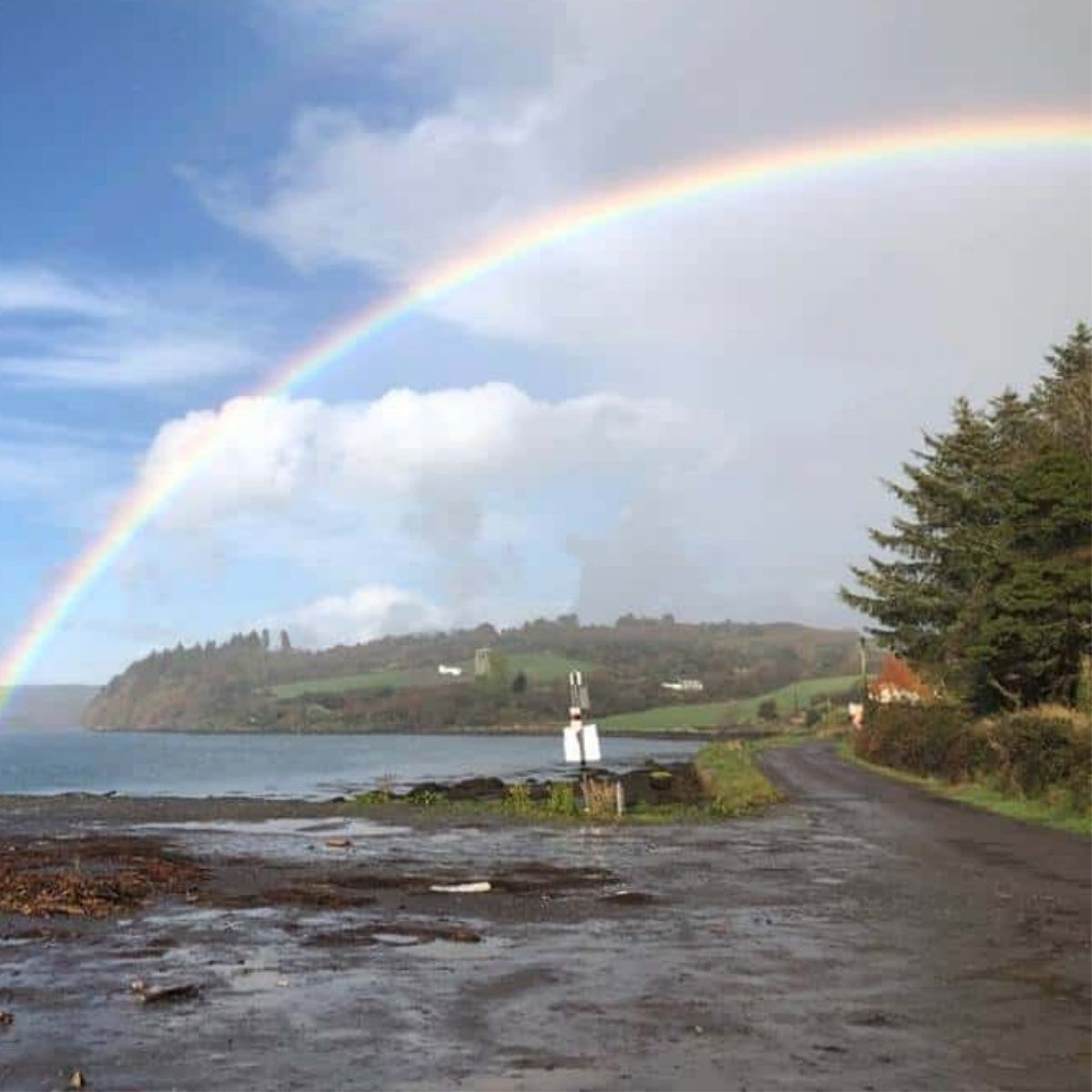 A rainbow in a cloudy and blue sky over the water and a pier in West Cork Ireland