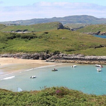 A sandy beach with mountains around it and boats in the cove